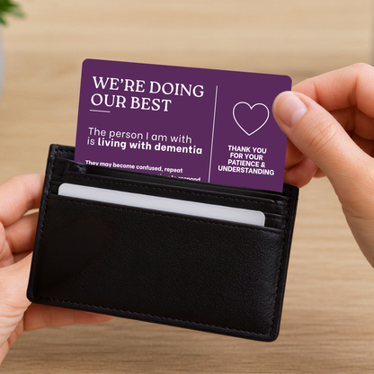 Person holding a black wallet with a purple dementia communication card inside, on a wooden surface.